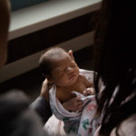 dimly lit portrait of a newborn being held by two people