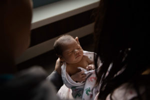 dimly lit portrait of a newborn being held by two people