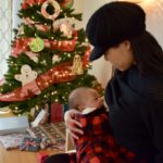 Woman breastfeeding her infant with a christmas tree and holiday decor in the foreground