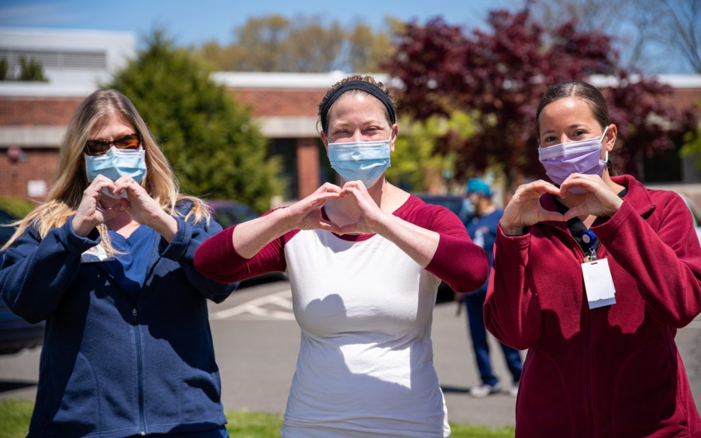 three healthcare professionals with face masks making heart symbol with hands