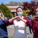 three healthcare professionals with face masks making heart symbol with hands