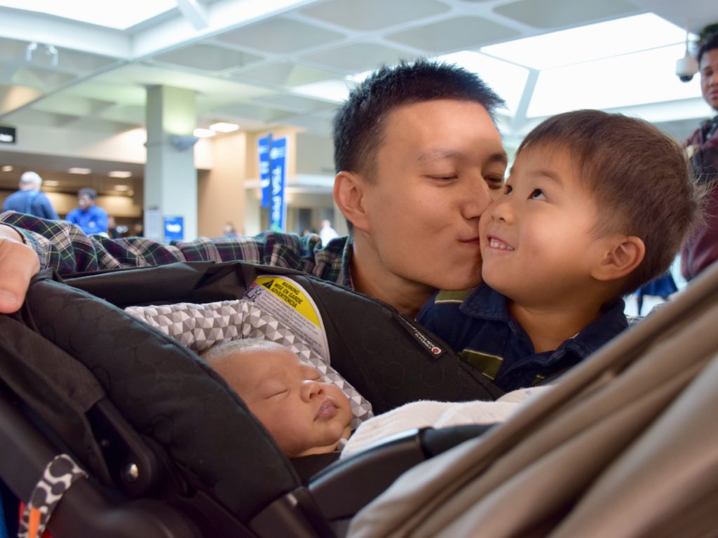 father kissing his son while overlooking an infant in the stroller