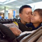 father kissing his son while overlooking an infant in the stroller