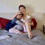 Photo of Chinese woman sitting on a bed with a small child laying on her left while breastfeeding an infant cradled in her left arm