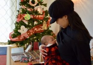 Woman breastfeeding her infant with a christmas tree and holiday decor in the foreground